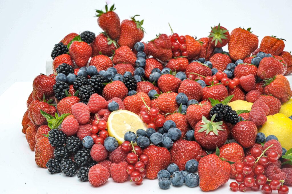 A dense, vibrant pile of fresh strawberries, blueberries, blackberries, raspberries, and red currants, accented with a few lemon slices.