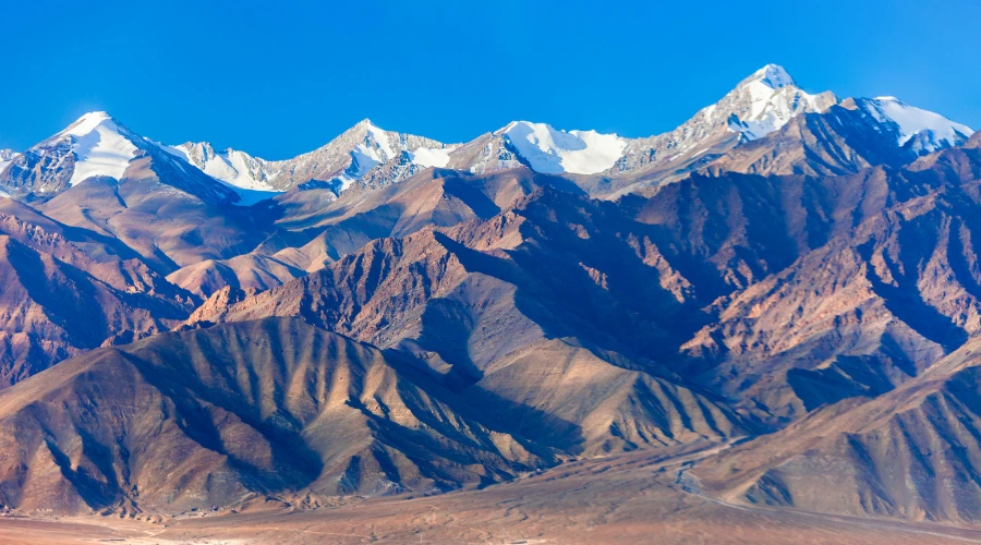 “Snow-capped Himalayan mountains in Leh Ladakh with rugged brown valleys and clear blue sky”