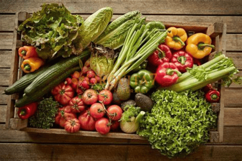 A wooden crate overflowing with organic greens, bell peppers, tomatoes, and avocados, showcasing the natural ingredients used in OroVita7.