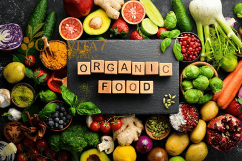 A black slate board with wooden blocks spelling "ORGANIC FOOD" surrounded by a colorful variety of organic berries, vegetables, and spices.