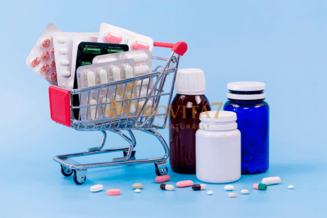 A small silver and red shopping cart filled with various blister packs of pills, sitting next to medicine bottles on a light blue background. The OROVITA7 logo is placed prominently in the center of the arrangement.
