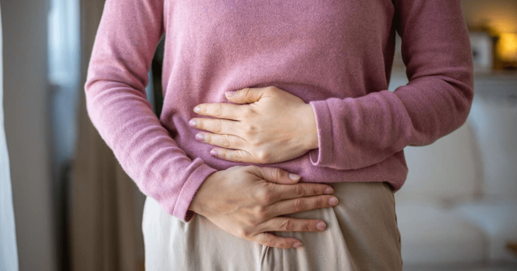 A woman clutching her midsection with both hands, suggesting symptoms of indigestion, bloating, or stomach cramps.