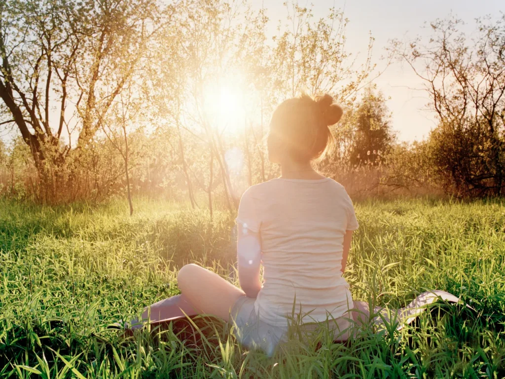 A woman meditating in a sun-drenched field to combat low energy and restore mental clarity during a bright morning.