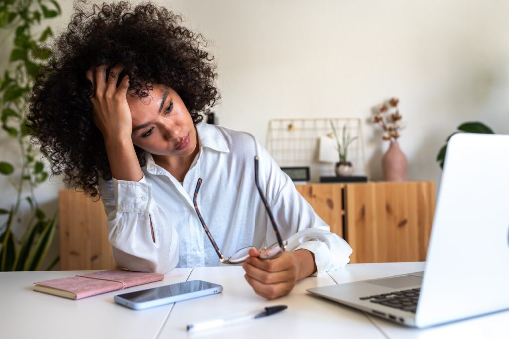 A tired woman leaning on her hand at a desk, looking overwhelmed by low energy while trying to focus on her laptop.