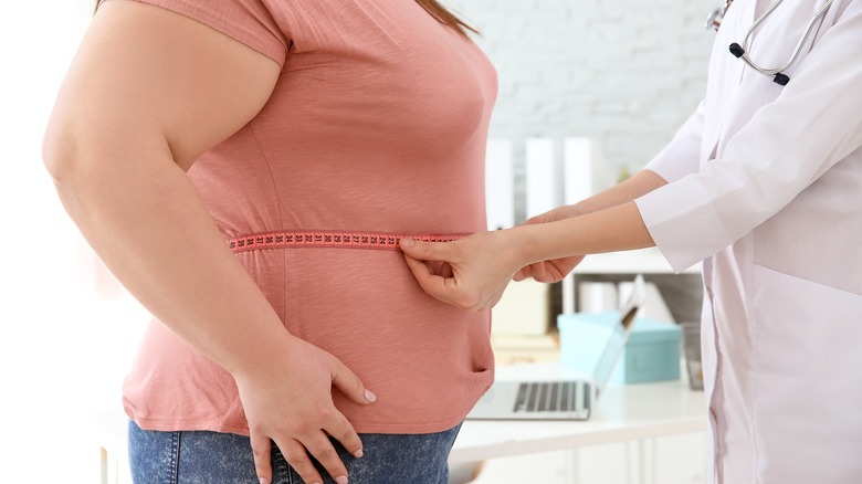 A healthcare provider measuring a patient’s waist circumference to assess health risks associated with obesity.