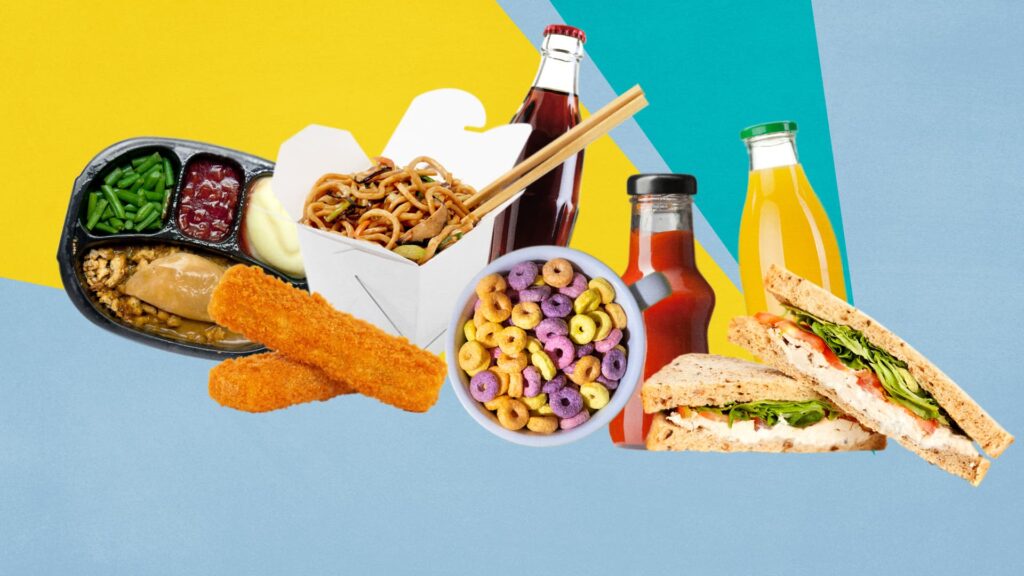 A top-down view of a white table overflowing with various high-calorie processed foods. The spread includes three large sesame seed burgers with lettuce and onion, a pile of french fries, potato chips, pretzels, pink frosted cupcakes, macarons, colorful chocolate candies, and several dipping sauces. The image highlights a variety of salty snacks and sugary desserts.